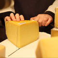 Cheesemonger hand cutting a wheel of Connage Gouda at Rennet & Rind.