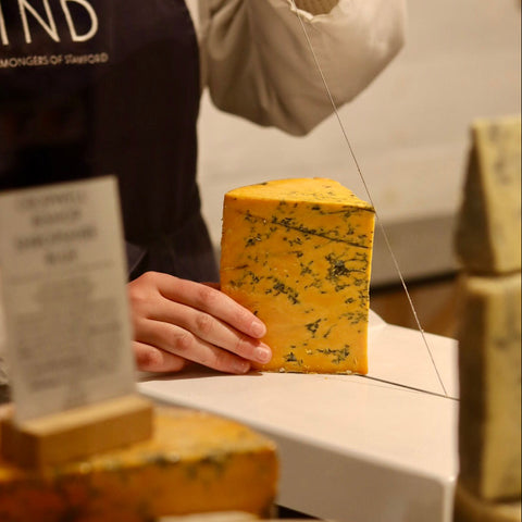 Cheesemonger hand cutting a wedge of Cropwell Bishop Shropshire Blue at Rennet & Rind.