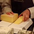 Cheesemonger hand cutting a wheel of Ogleshield at Rennet & Rind